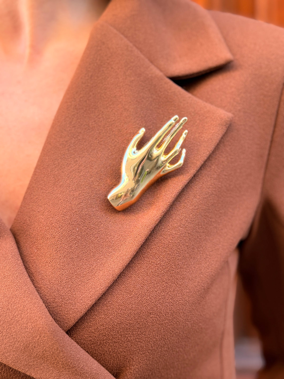 Spilla donna dorata a forma di mano indossata su blazer